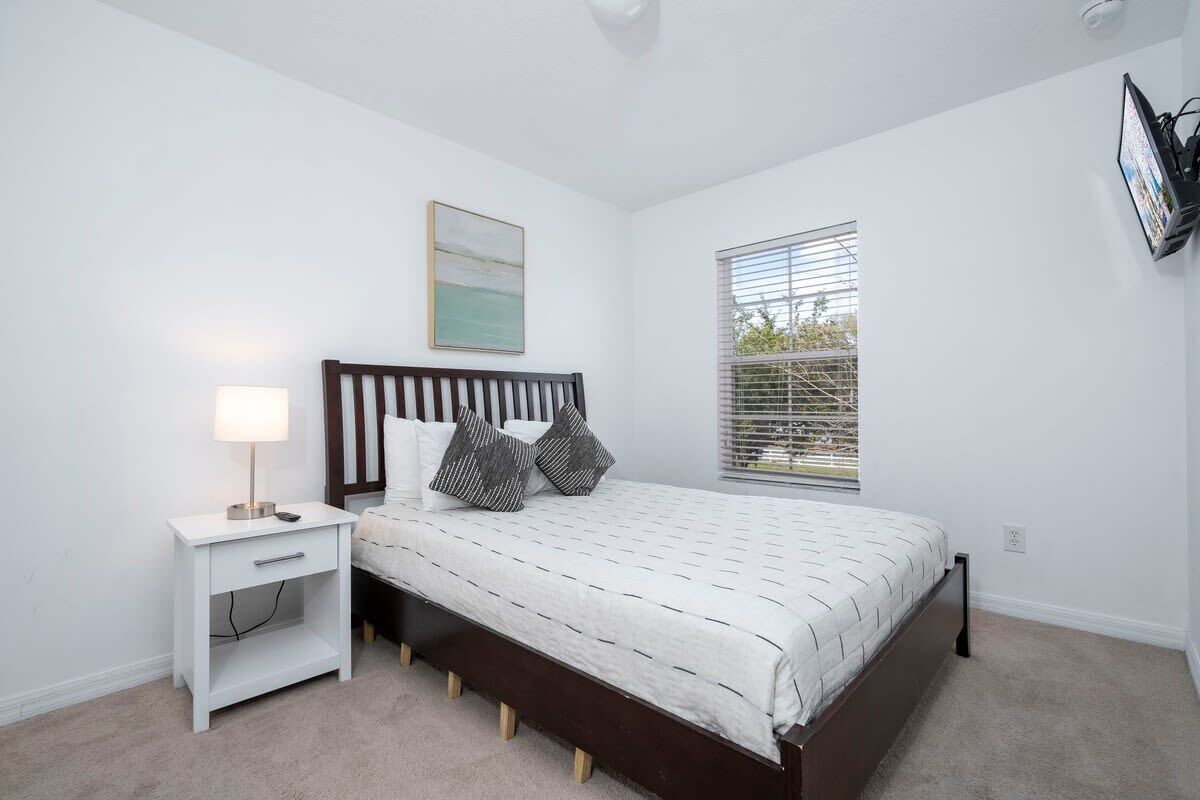 A bedroom with a bed, nightstand, lamp, and a window with blinds.
