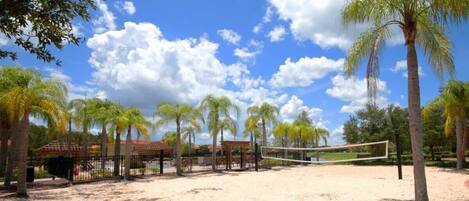 A beach volleyball court with palm trees and a gazebo in the background.