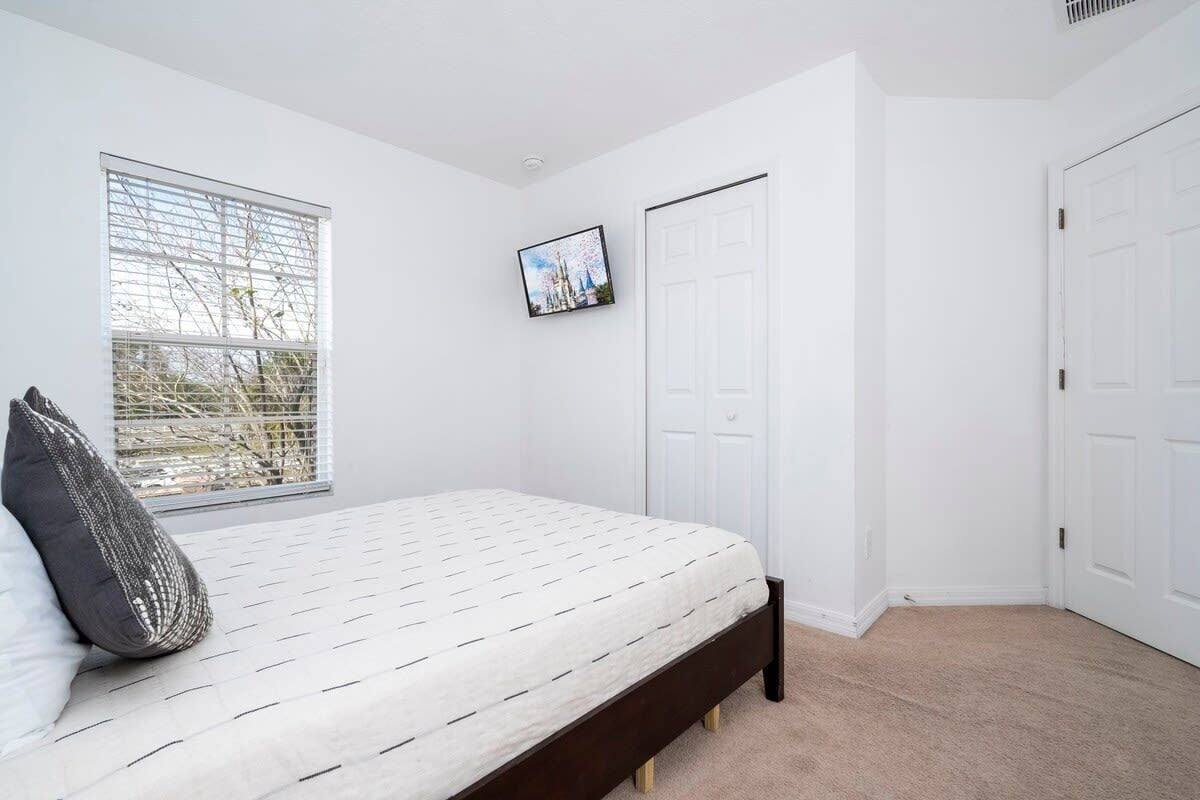 A bedroom with a bed, a window with blinds, a door, and a framed picture on the wall.