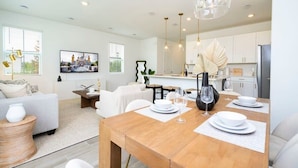 A modern kitchen with white cabinets, a dining table set for four, and pendant lighting. - Casa Serene 3Bd near Disney @Festival Resort 963 (Davenport)