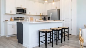 A modern kitchen with white cabinetry, a stainless steel refrigerator, and a central island with bar stools. - Casa Serene 3Bd near Disney @Festival Resort 963 (Davenport)