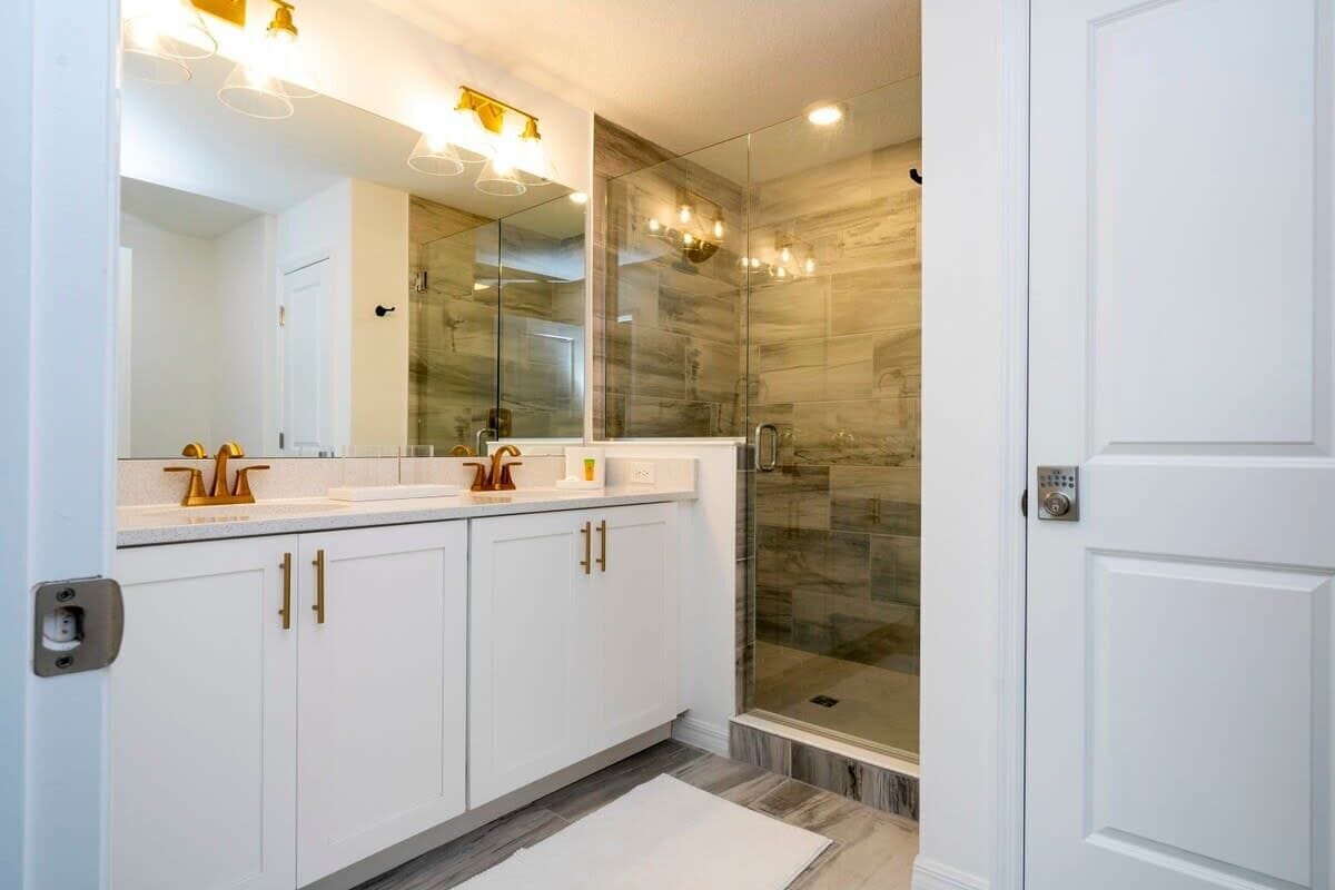 Un bagno moderno con uno specchio grande, mobili bianchi e un box doccia in vetro.