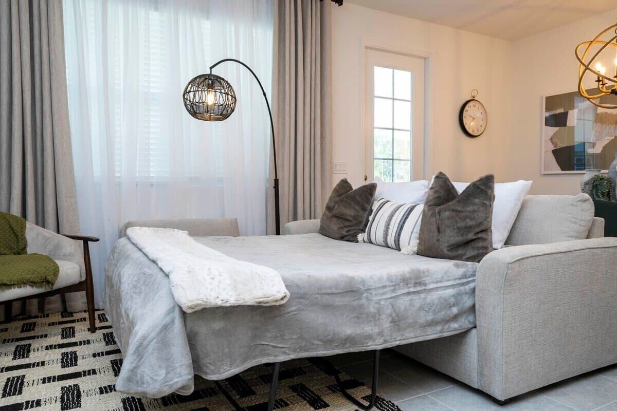 A modern bedroom with a bed, a sofa, a chair, and a large window with curtains.