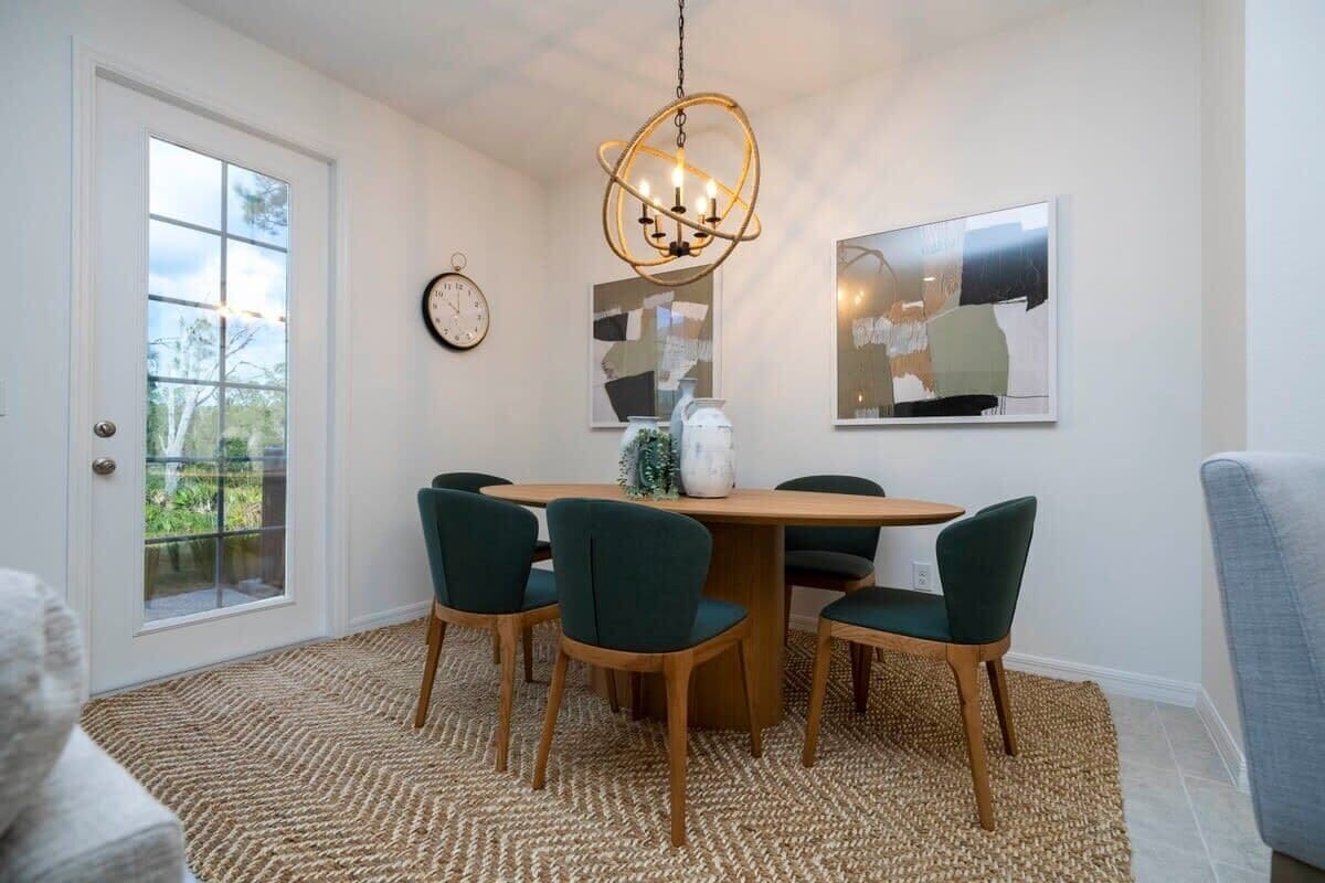 A dining area with a wooden table, six chairs, a woven rug, a chandelier, and abstract art on the walls.