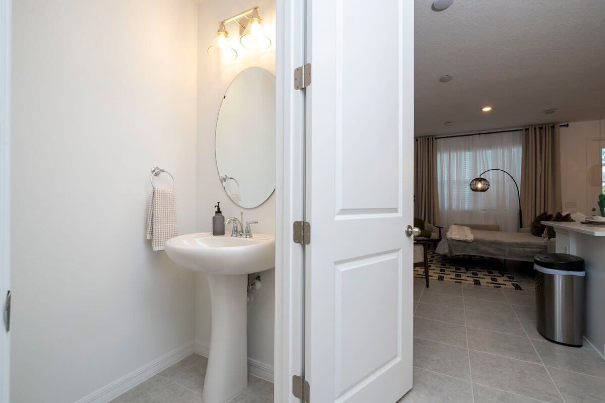 A modern bathroom with a pedestal sink, a round mirror, and a towel rack.