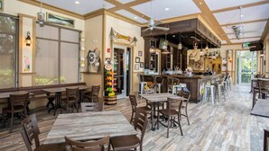 Een ruime restaurantruimte met hoge plafonds, houten tafels en stoelen, een bar en een groot raam dat voor natuurlijk licht zorgt.