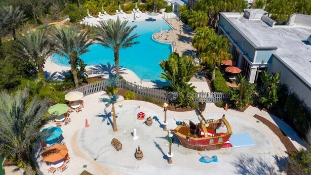 Een resort met een groot zwembad, palmbomen en een waterattractie in de vorm van een boot.