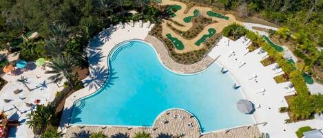 Vista aérea de un resort con una gran piscina, tumbonas y áreas ajardinadas.