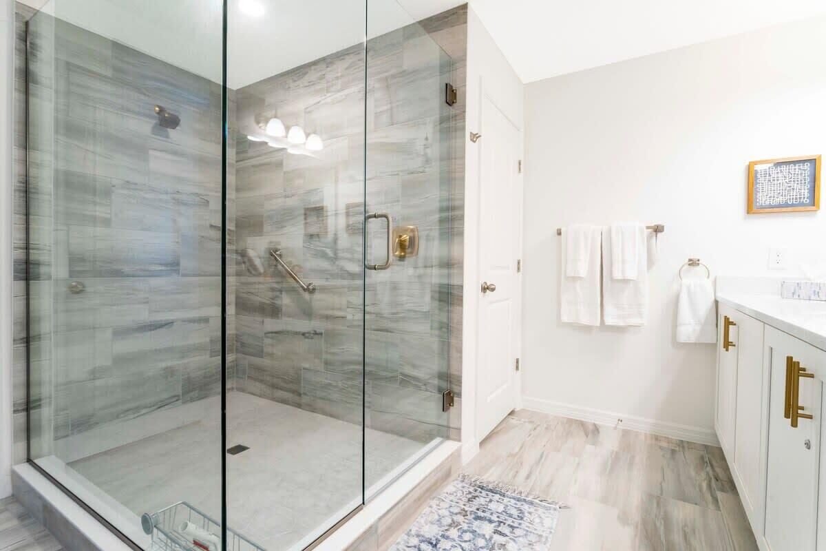 Ein modernes Badezimmer mit einer in Glas abgeschlossenen Dusche, weißen Schränken und einem gemusterten Teppich.