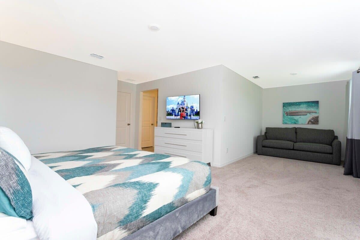 Een slaapkamer met een bed, een televisie, een bank en een schilderij aan de muur.