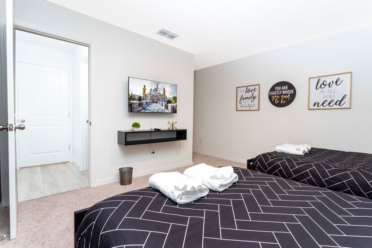 A hotel room with two beds, a TV mounted on the wall, and motivational wall art.
