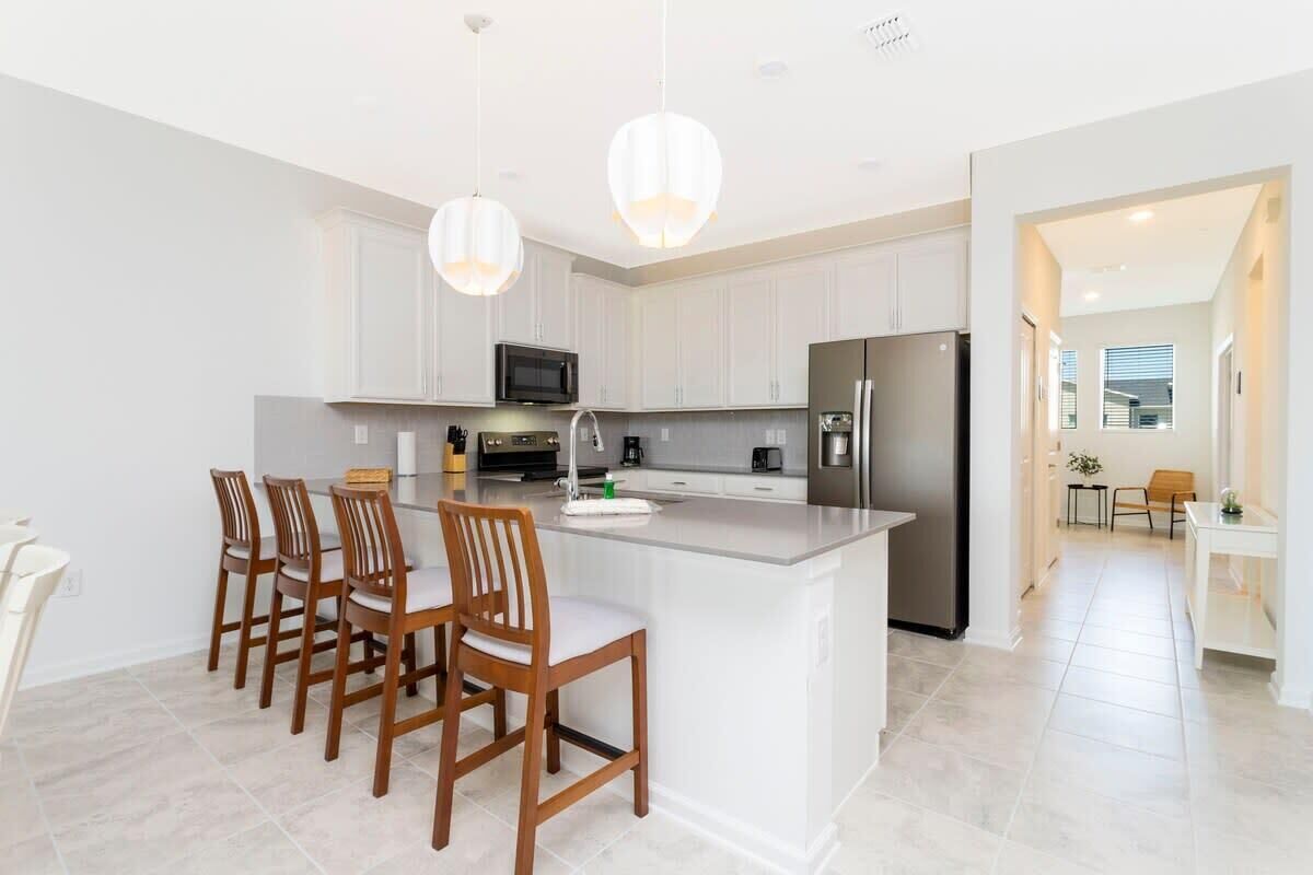 A modern kitchen with white cabinetry, a central island with bar stools, stainless steel appliances, and pendant lighting.