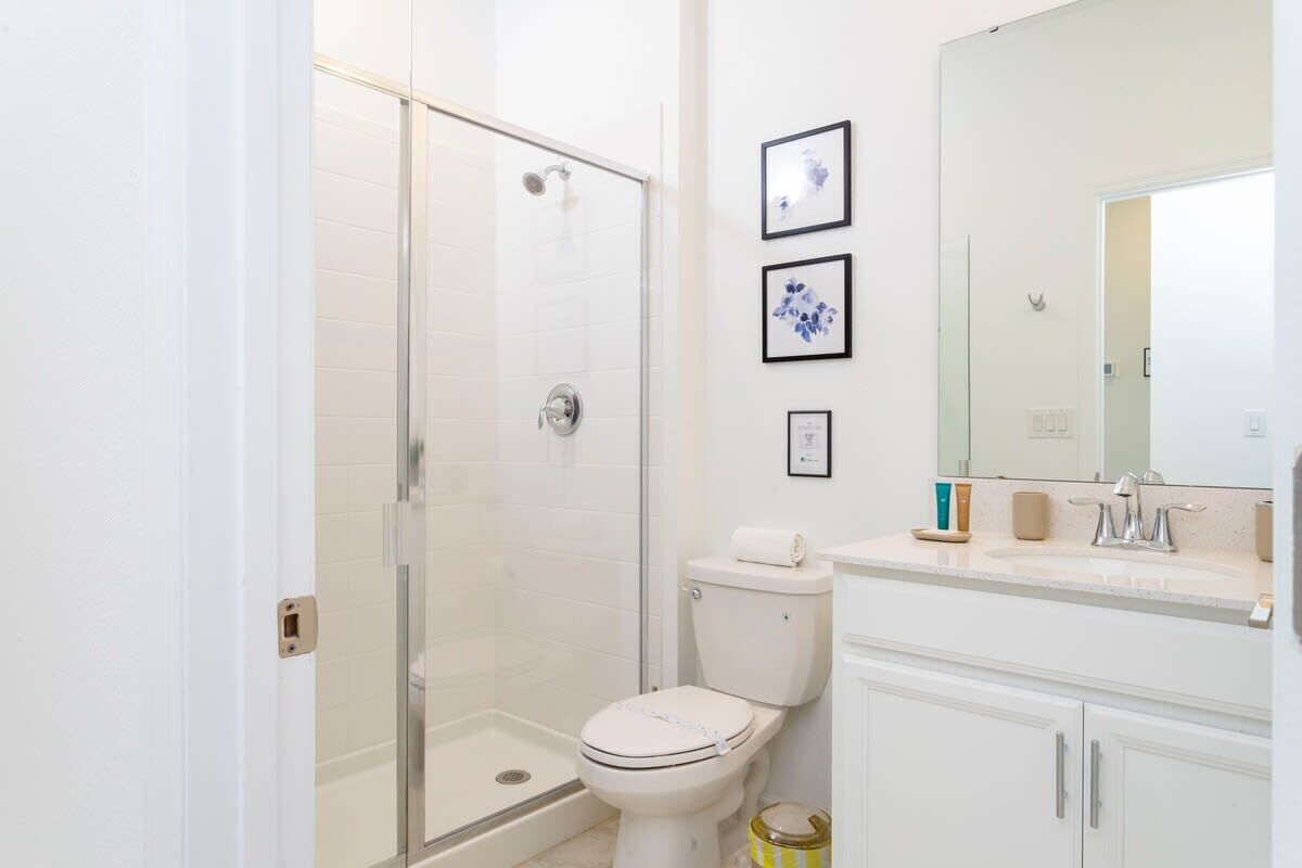 A bathroom with a glass-enclosed shower, a toilet, and a sink with a mirror.