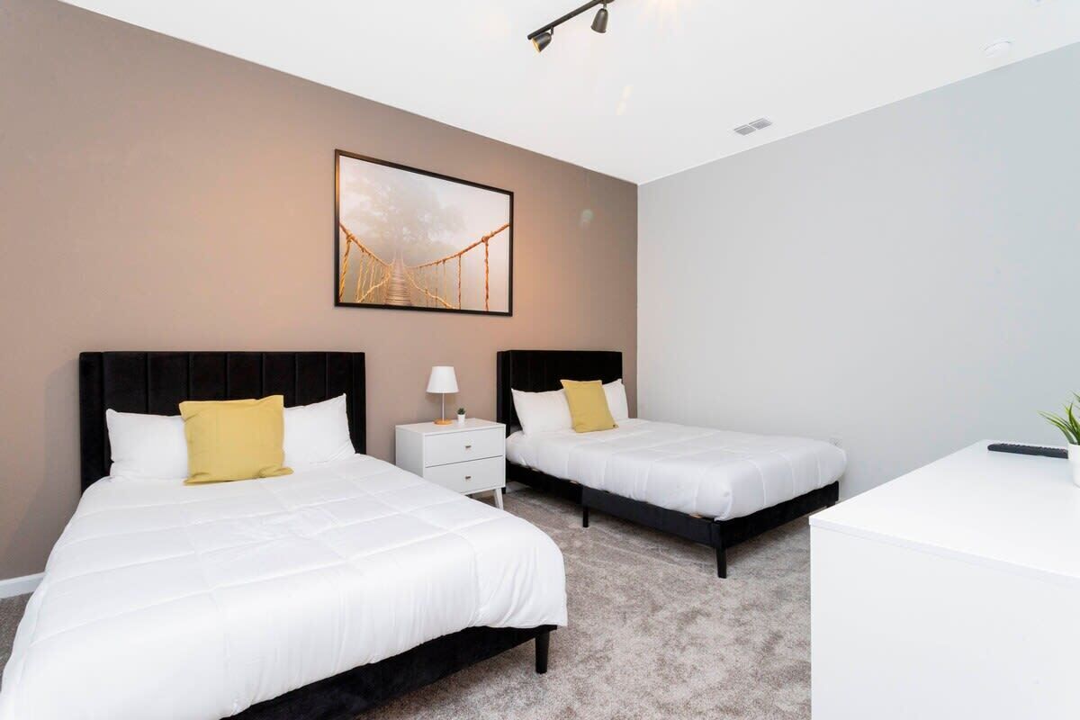 A hotel room with two beds, a white desk, and a framed picture on the wall.