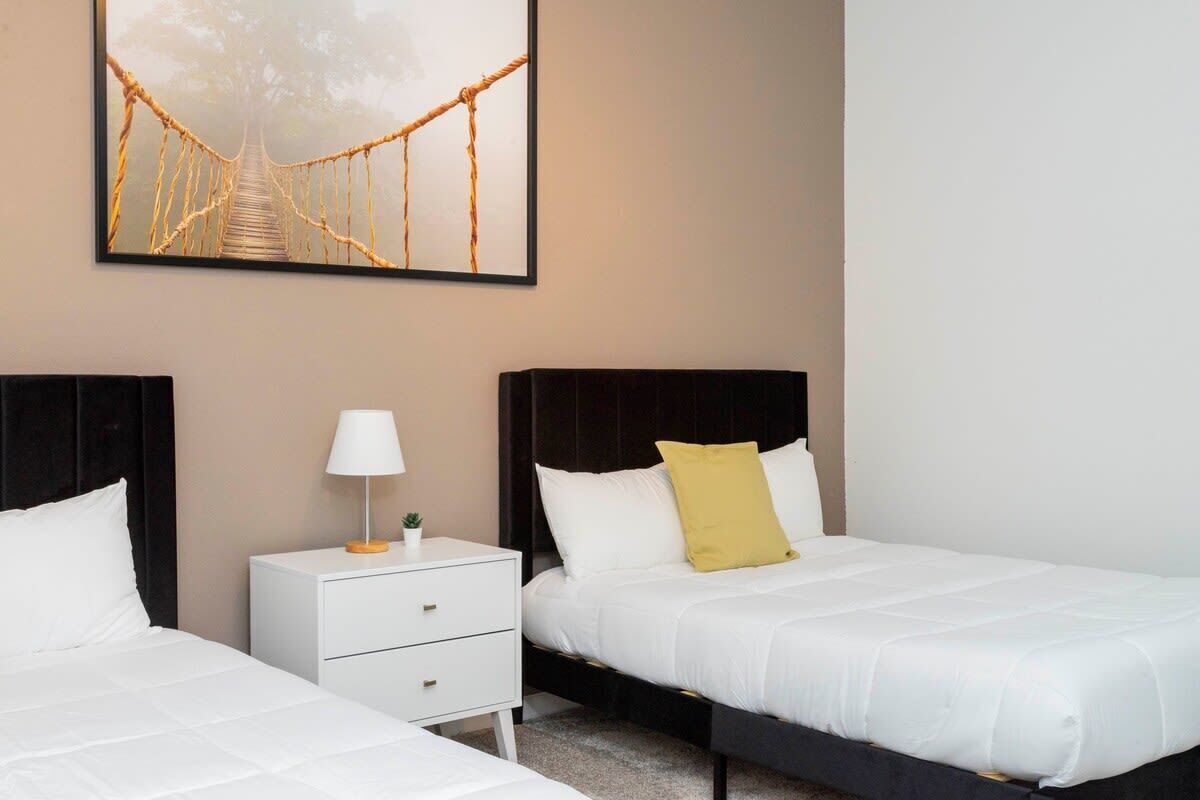 A hotel room with two beds, a nightstand with a lamp, and a framed picture of a bridge.