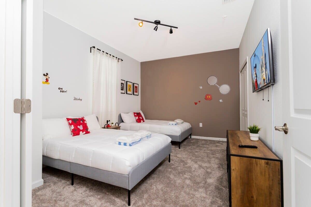 A modern bedroom with two beds, a small wooden side table, a TV, and a wall with decorative stickers.