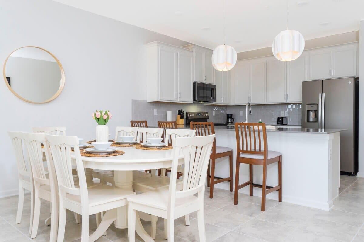A modern kitchen with white cabinetry, a central island, and a dining area with white chairs.