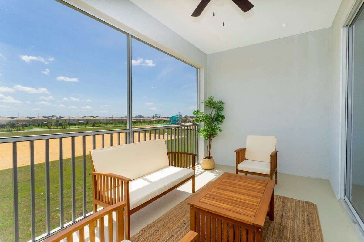 A balcony with a sofa, chairs, and a table, overlooking a grassy area with a clear sky.