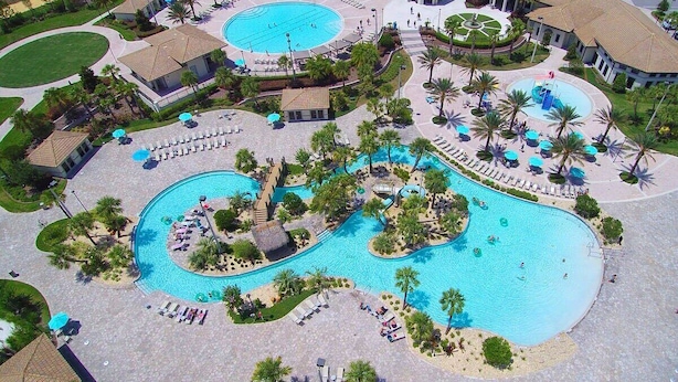 Vue aérienne d’un complexe hôtelier doté de plusieurs piscines, de chaises longues et de palmiers.