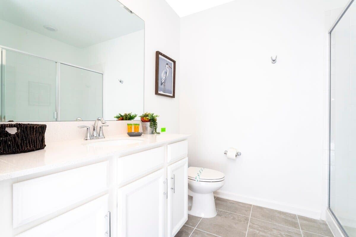 A modern bathroom with a white vanity, a large mirror, a toilet, and a shower area.