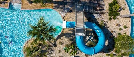 An aerial view of a swimming pool area with a water slide, palm trees, and a stone pathway.
