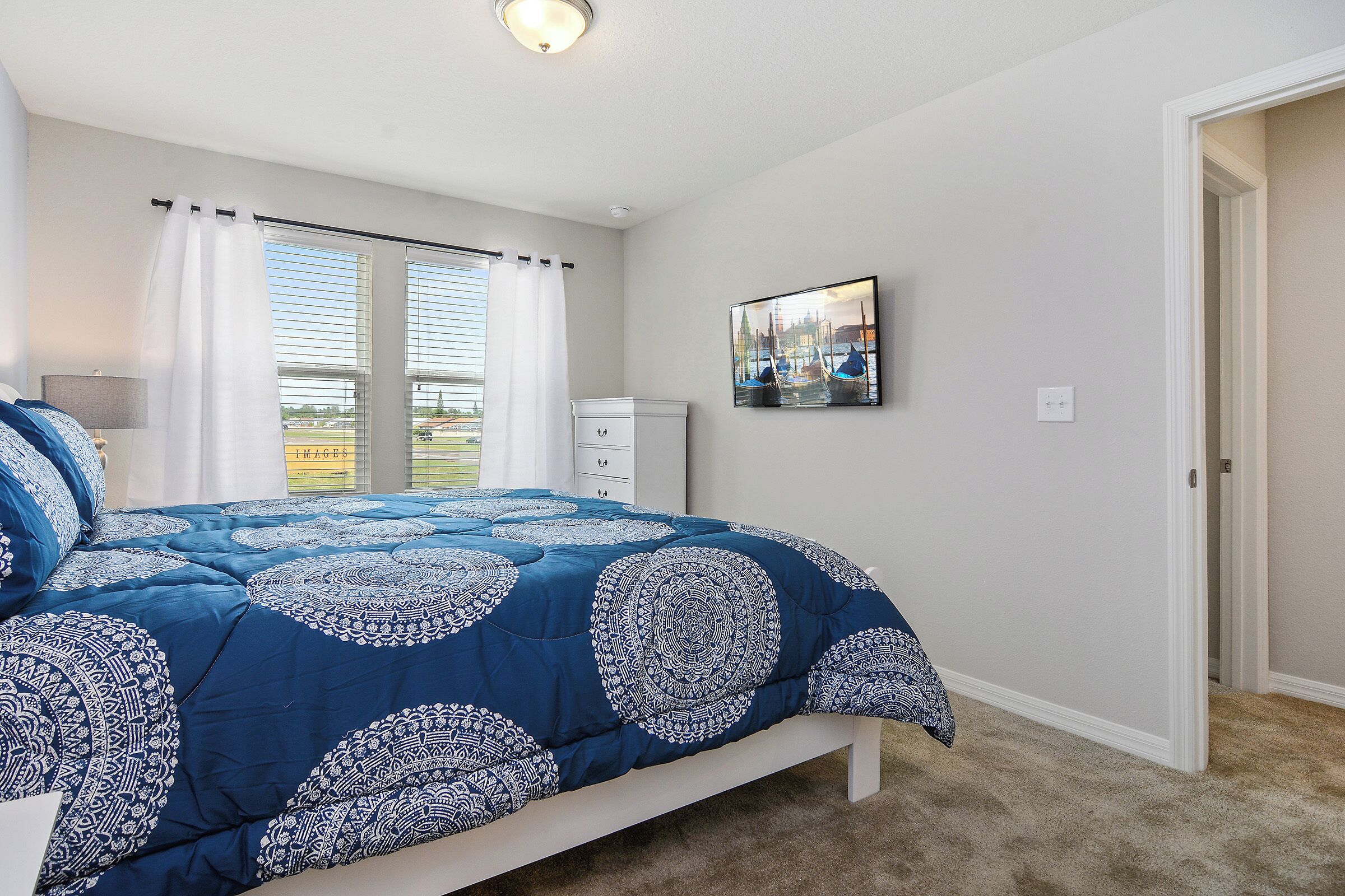 A bedroom with a large bed, a nightstand, a dresser, a window with curtains, and a painting on the wall.