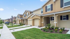 A row of townhouses with attached garages, a sidewalk, and a landscaped front yard. - Family Friendly Four Bedroom w GameRoom @Disney 5145 (Kissimmee)