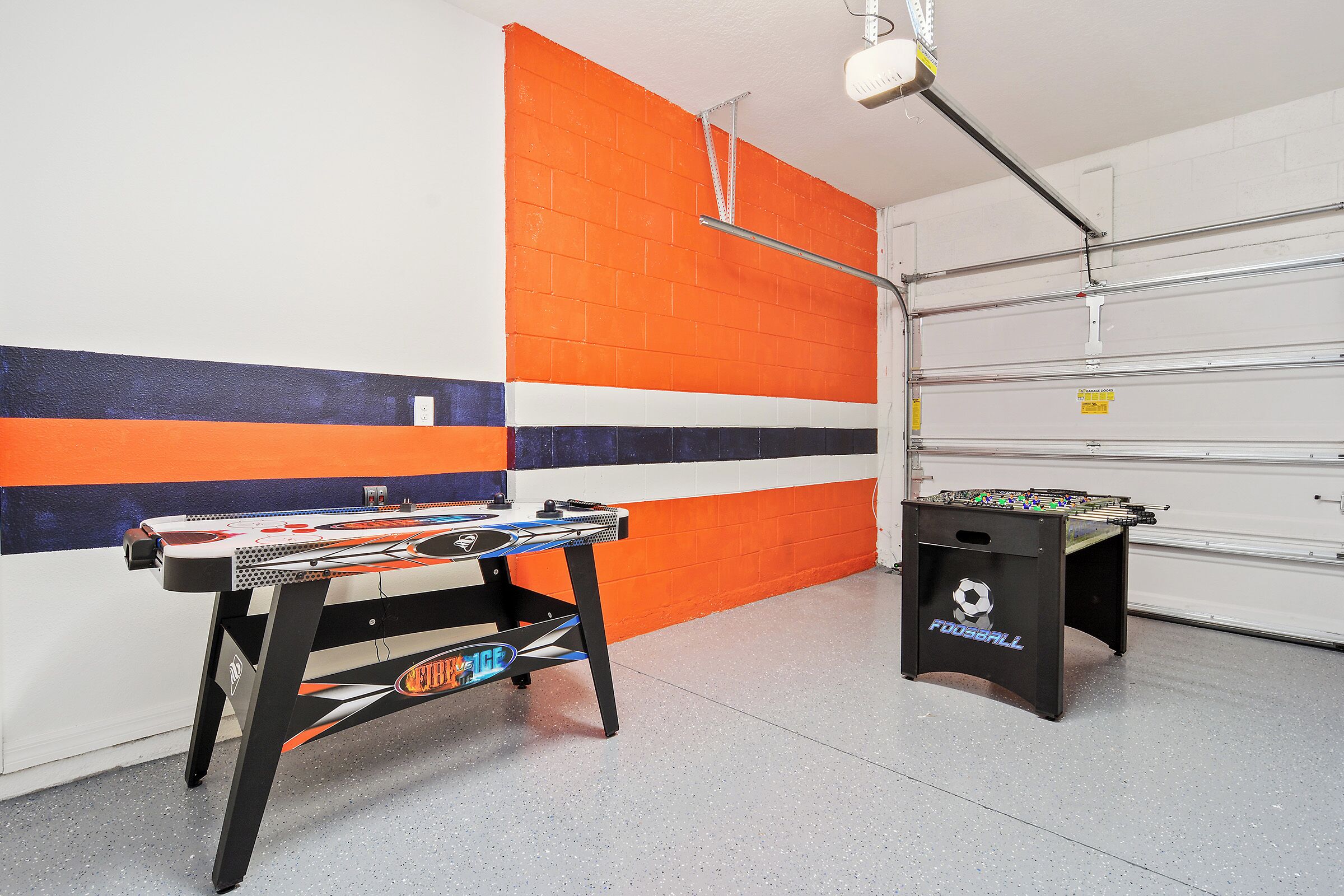 A room with a foosball table and a table tennis table against a wall with a striped pattern.