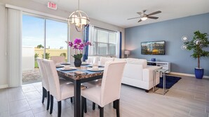 A modern living room with a dining area, a ceiling fan, and a large window with blinds. - Family Friendly Four Bedroom w GameRoom @Disney 5145 (Kissimmee)