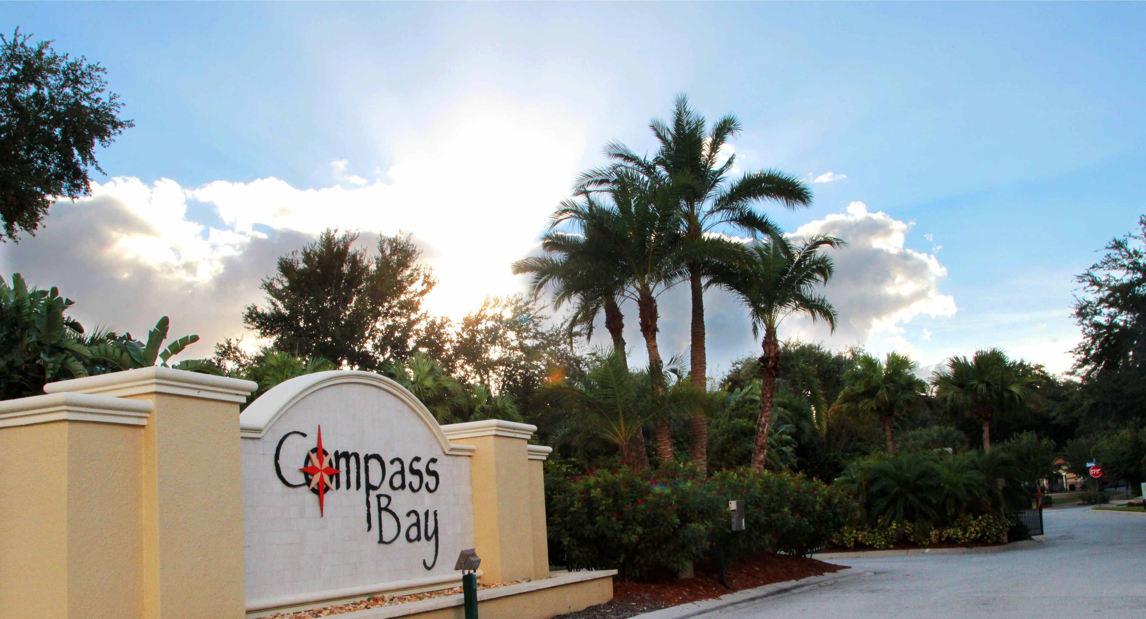 A sign for Compass Bay with a palm tree and a clear sky in the background.