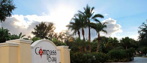 A sign for Compass Bay with a palm tree and a clear sky in the background.