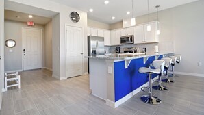 A modern kitchen with white cabinets, a blue island, stainless steel appliances, and bar stools. - Family Friendly Four Bedroom w GameRoom @Disney 5145 (Kissimmee)