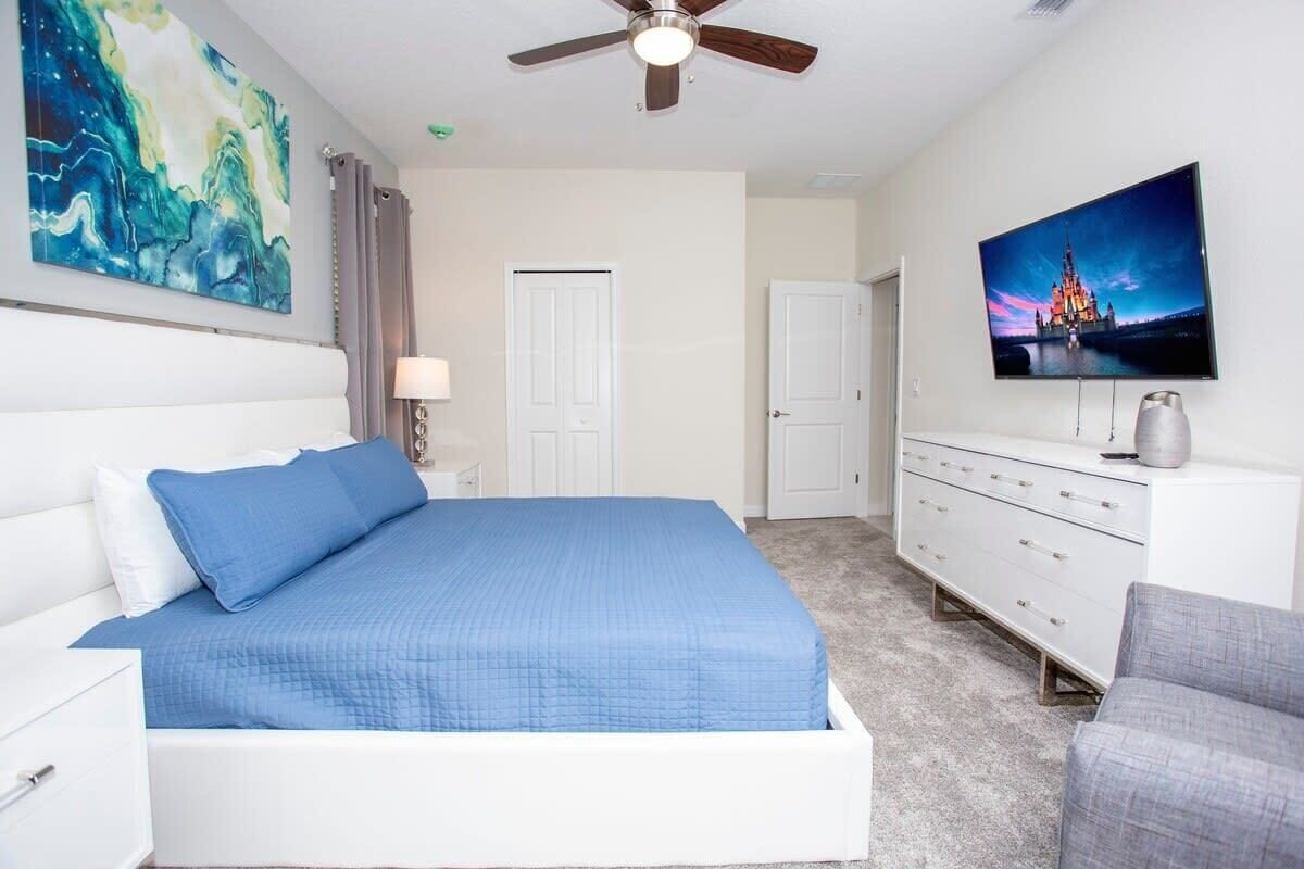 A bedroom with a bed, a TV, a ceiling fan, and a dresser.