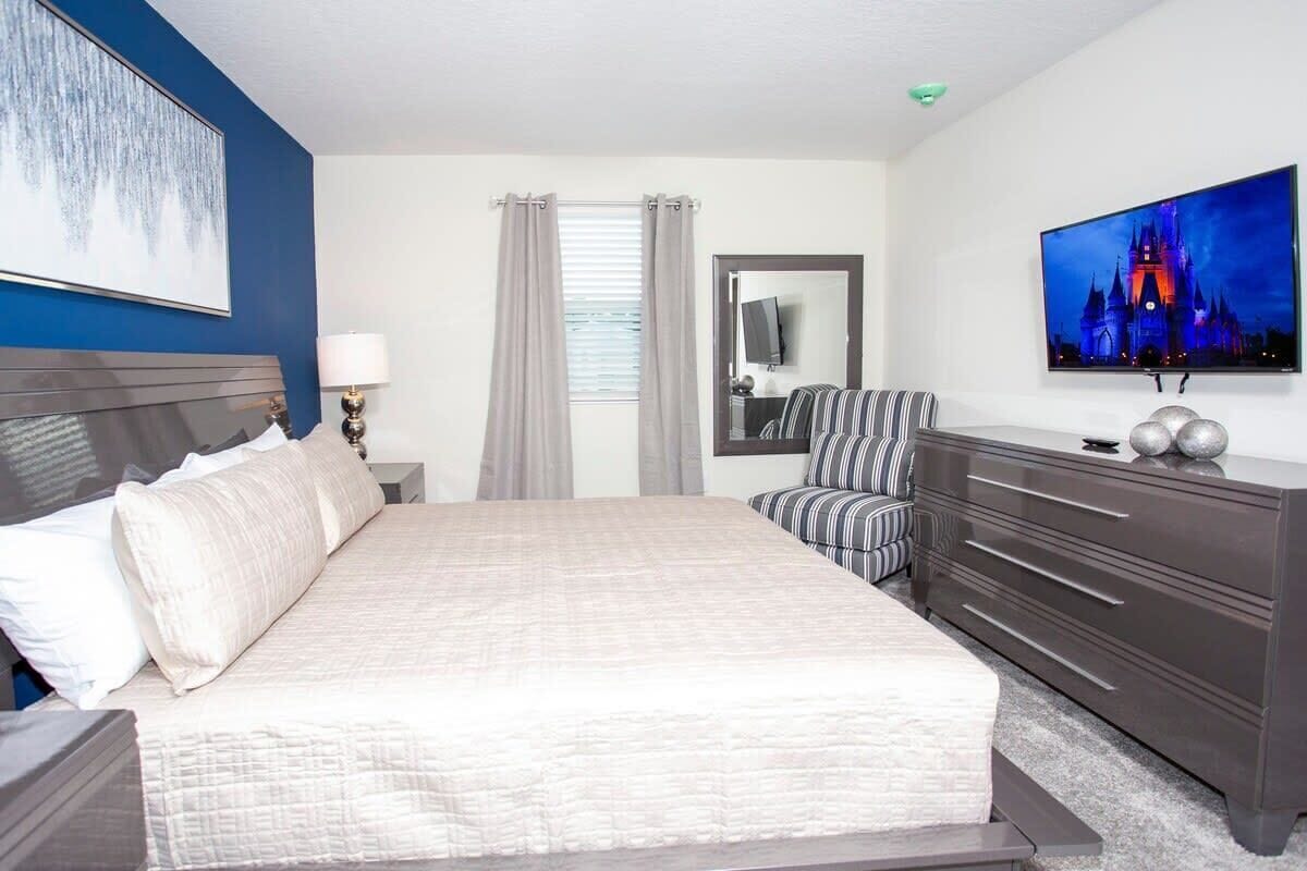 A hotel room with a large bed, a TV, a dresser, and a window with curtains.
