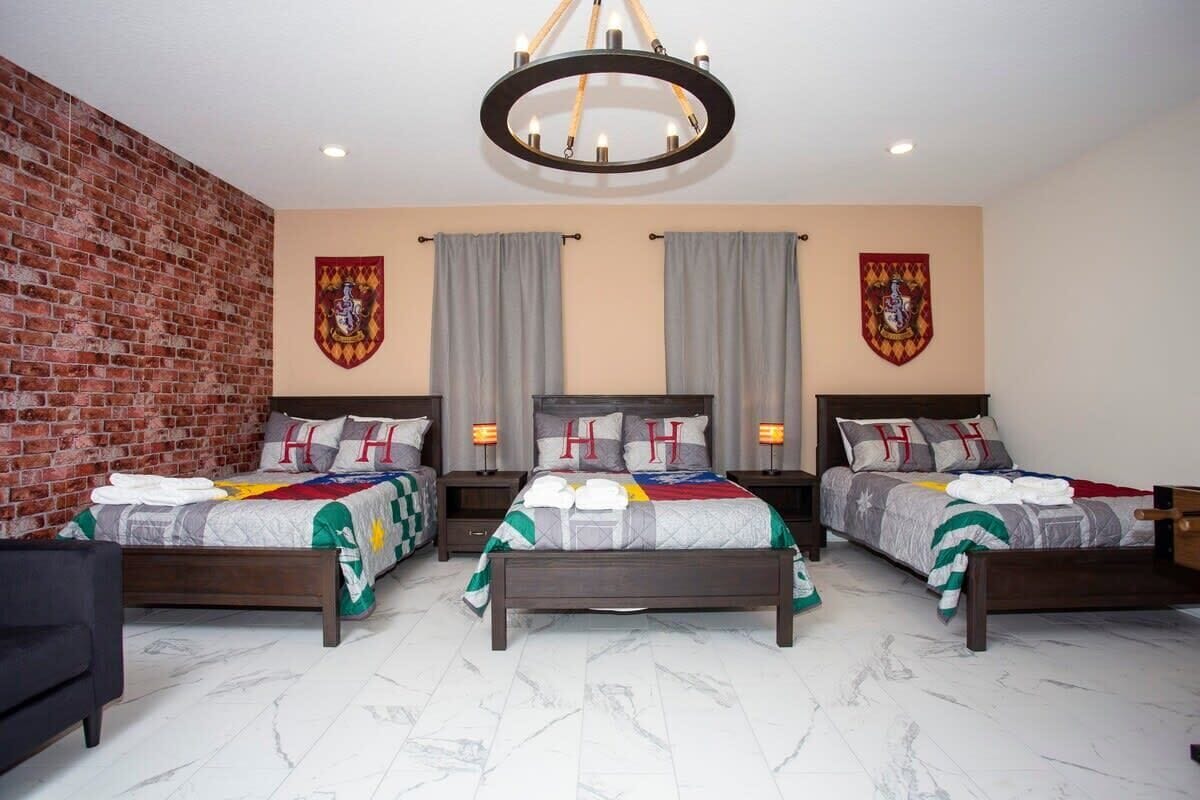 A hotel room with three beds, a brick wall, and two large windows with curtains.