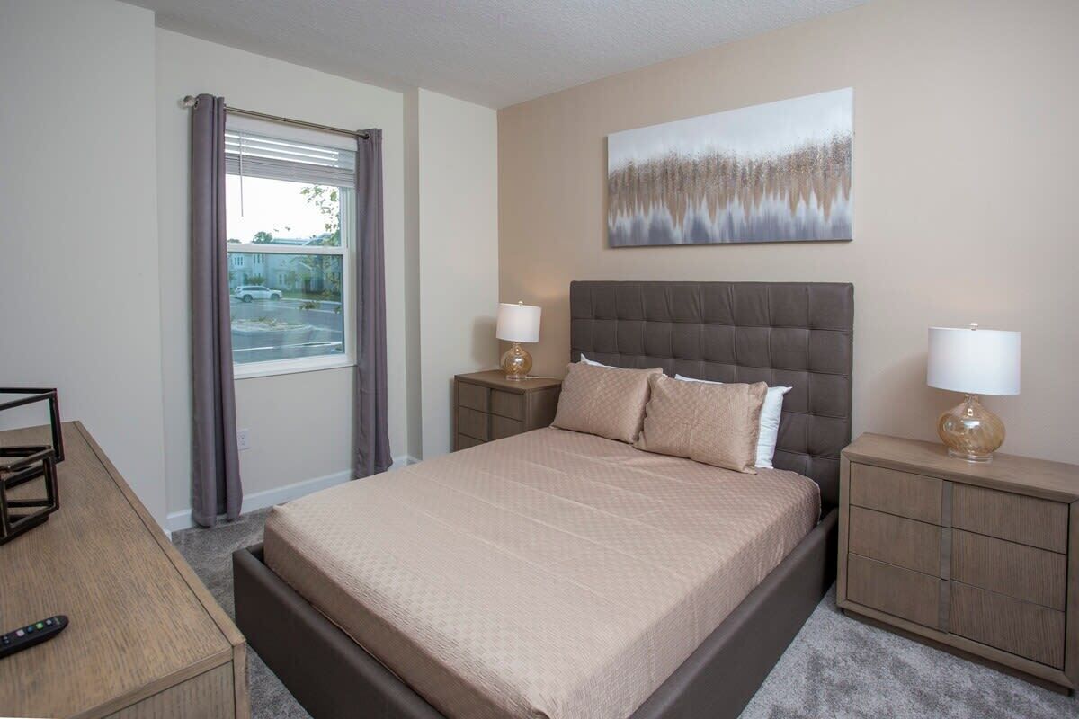 A hotel room with a large bed, two bedside tables with lamps, a painting on the wall, and a window with curtains.