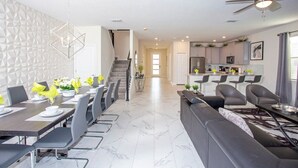 Una cocina moderna con una isla central, un comedor con una mesa larga y sillas, y una sala de estar con un sofá y una mesa de centro.