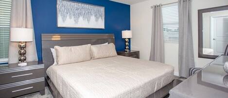 A bedroom with a large bed, two bedside tables with lamps, a headboard, and a painting on the wall.
