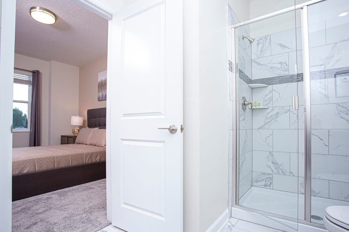 A hotel room with a bed, a nightstand, a bedside lamp, a shower with glass doors, and a toilet.