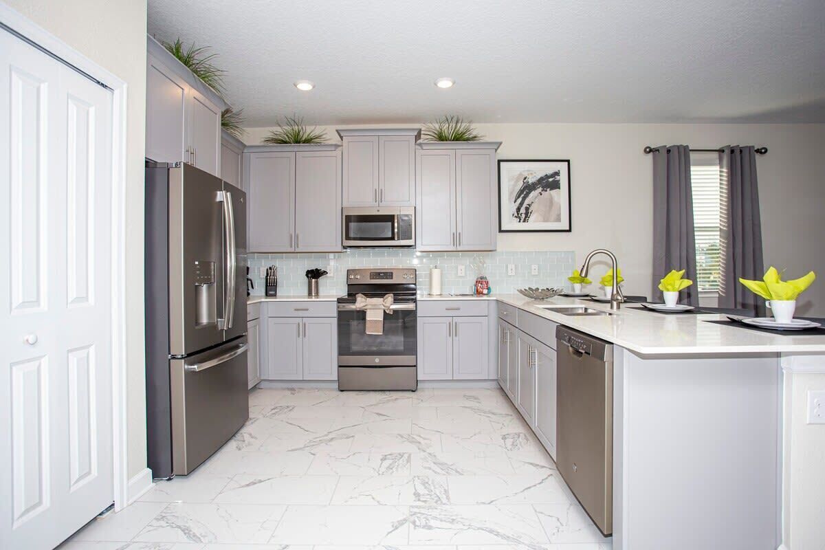 A modern kitchen with stainless steel appliances, light grey cabinets, and a marble floor.