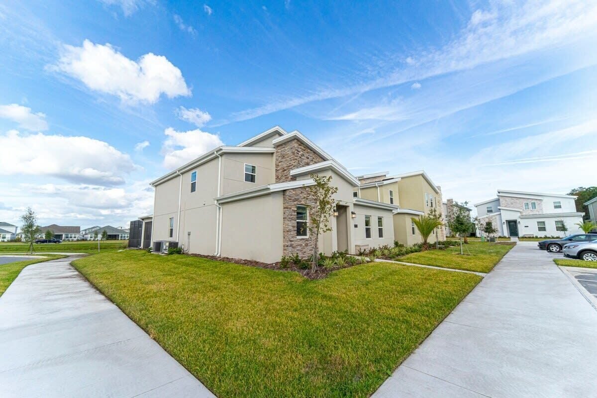 A modern residential building with a stone facade, a well-maintained lawn, and a clear sky.