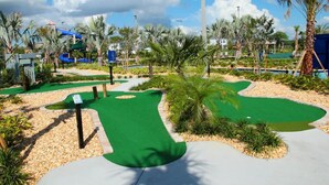 A golf course with a green putting area, palm trees, and a water slide in the background. - Gorgeous 2Bd Apto Close to Disney @ Storey Lake 404 3191 (Kissimmee)