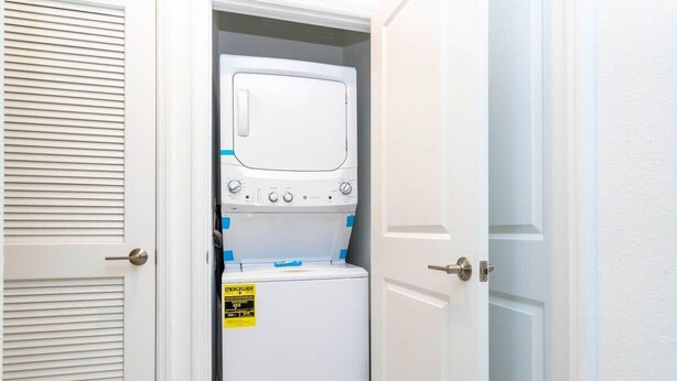 A compact washer and dryer unit with a visible energy efficiency label, housed in a narrow hallway with white doors. - Gorgeous 2Bd Apto Close to Disney @ Storey Lake 404 3191 (Kissimmee)