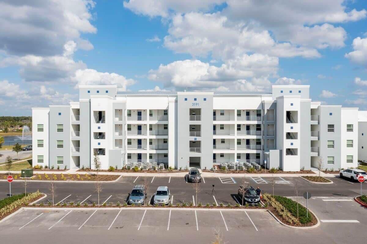 A modern multi-story hotel with a central courtyard, parking lot, and a clear sky.