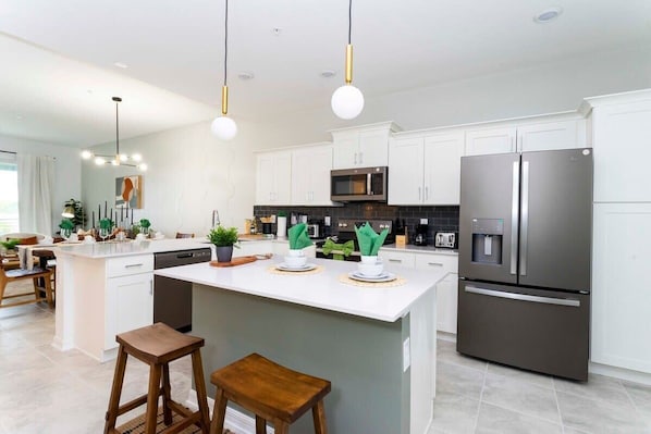 A modern kitchen with white cabinets, stainless steel appliances, and a central island with stools.