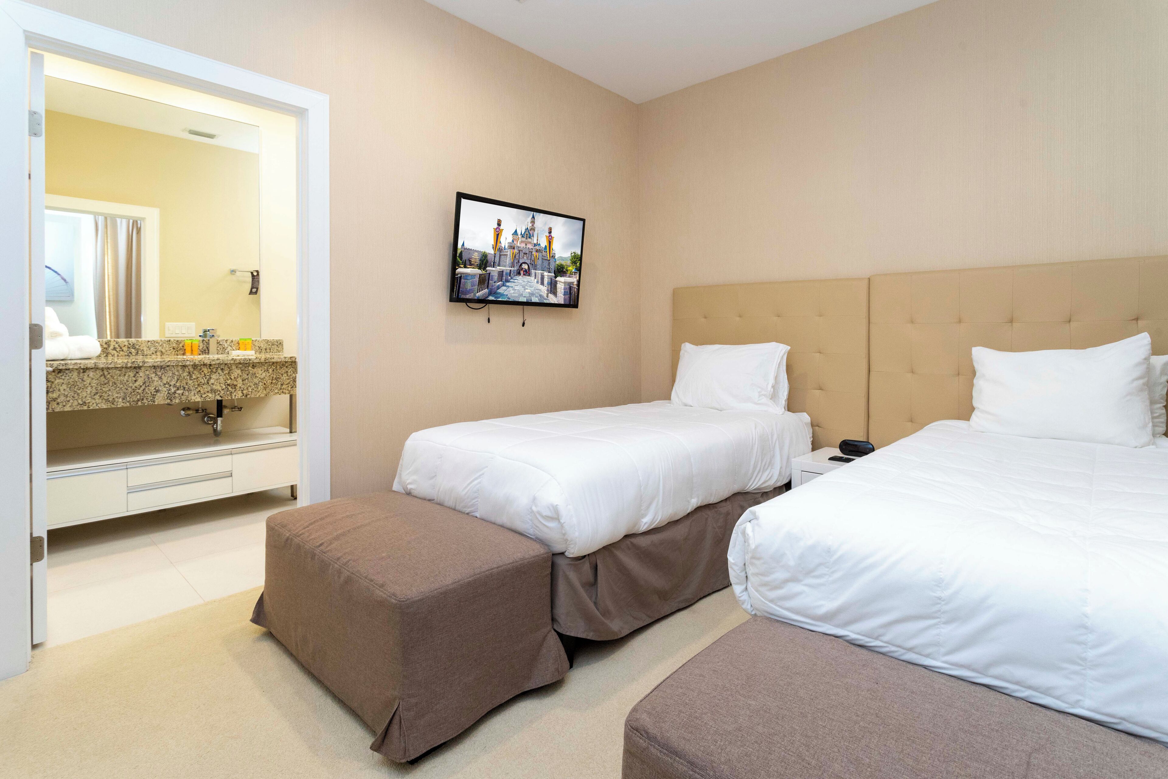 Quarto de hotel com duas camas, um espelho grande, televisão e banheiro com pia e amenities.