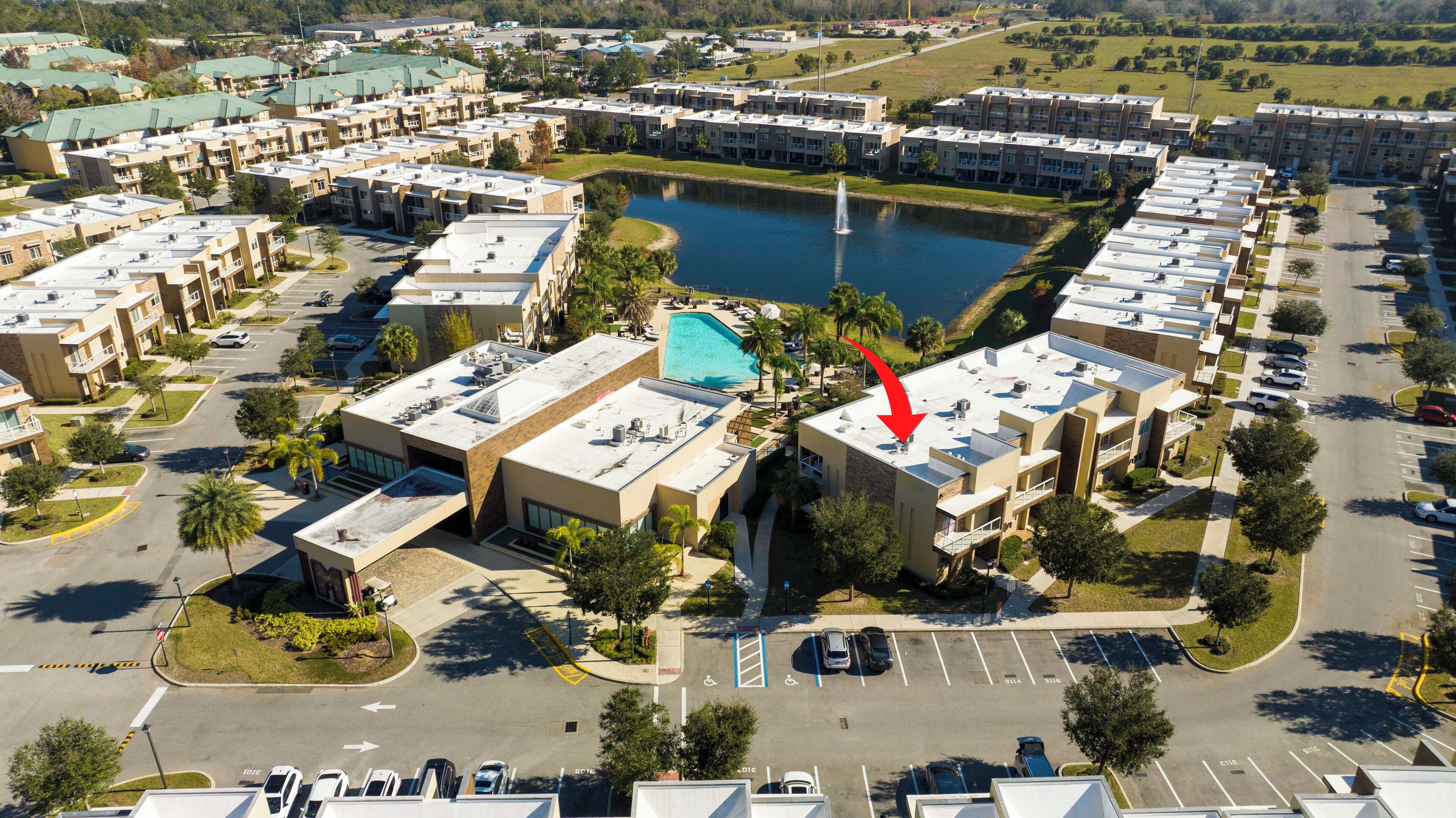An aerial view of a hotel complex with multiple buildings, a central swimming pool, and a lake.