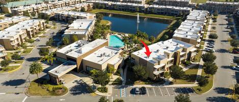 An aerial view of a hotel complex with multiple buildings, a central swimming pool, and a lake.