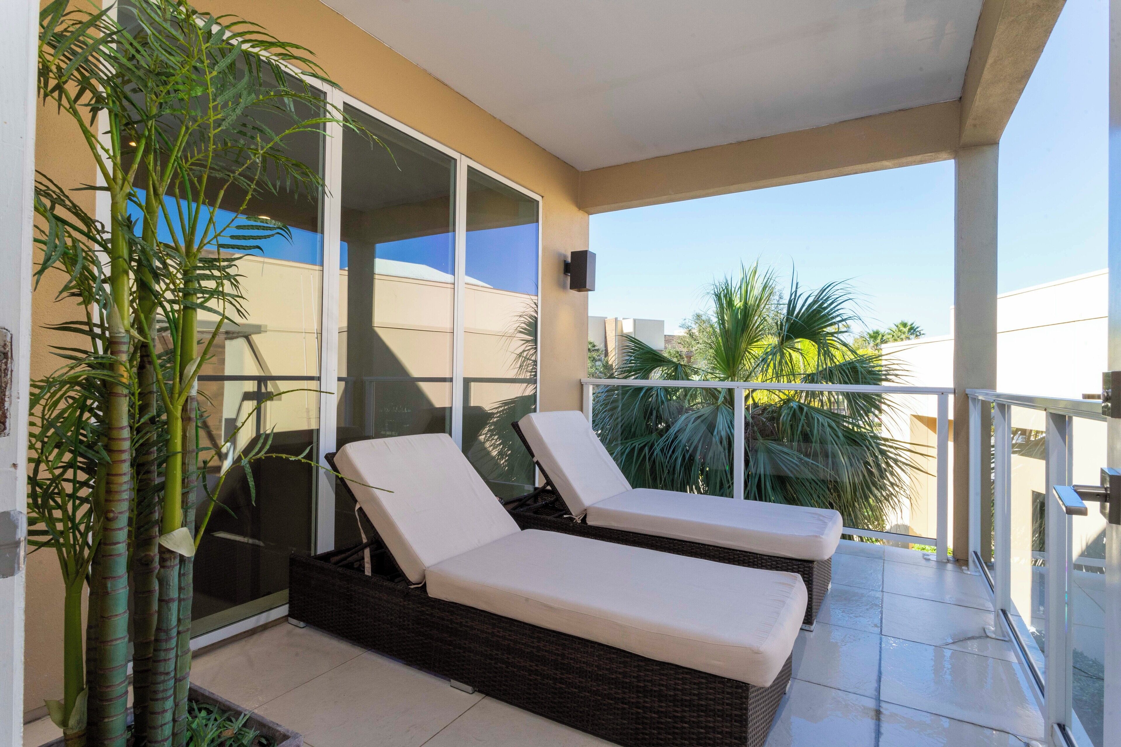 A balcony with two lounge chairs, a potted plant, and a glass door leading to a room.