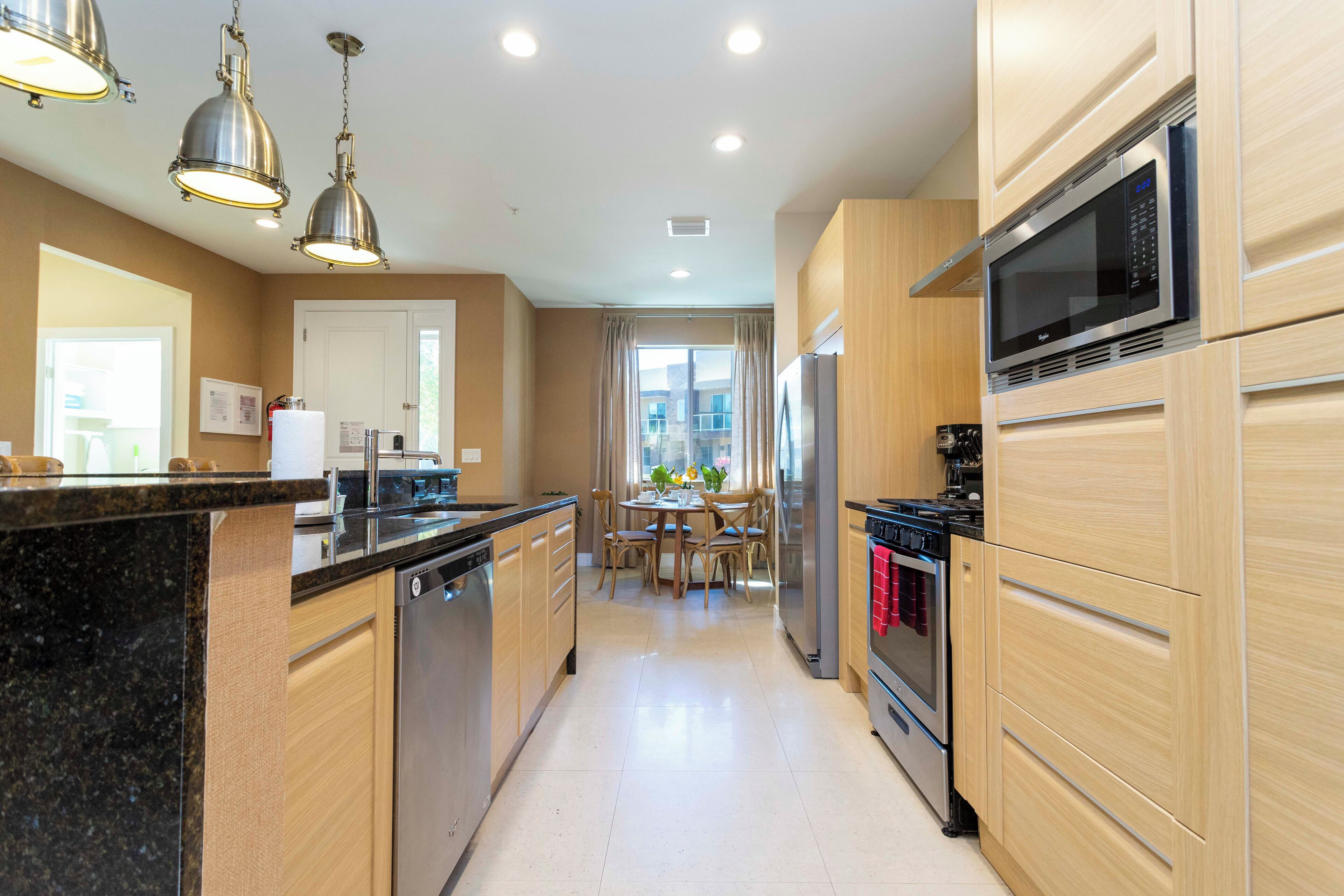 A modern kitchen with wooden cabinets, stainless steel appliances, and pendant lighting.